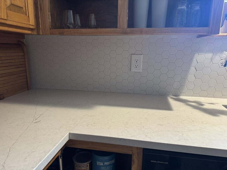 Kitchen corner with white hexagon tile backsplash, light marbled stone look countertop, and wood cabinets
