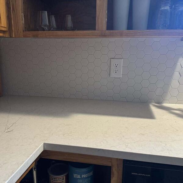 Kitchen corner with white hexagon tile backsplash, light marbled stone look countertop, and wood cabinets