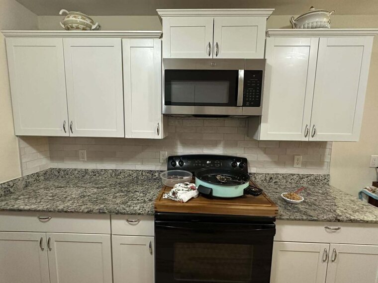 Kitchen with white cabinets, speckled granite counters, tile backsplash, black range and stainless microwave