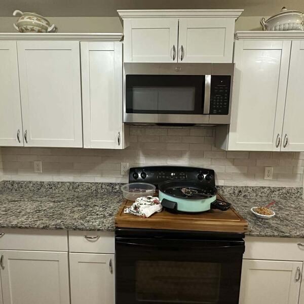 Kitchen with white cabinets, speckled granite counters, tile backsplash, black range and stainless microwave