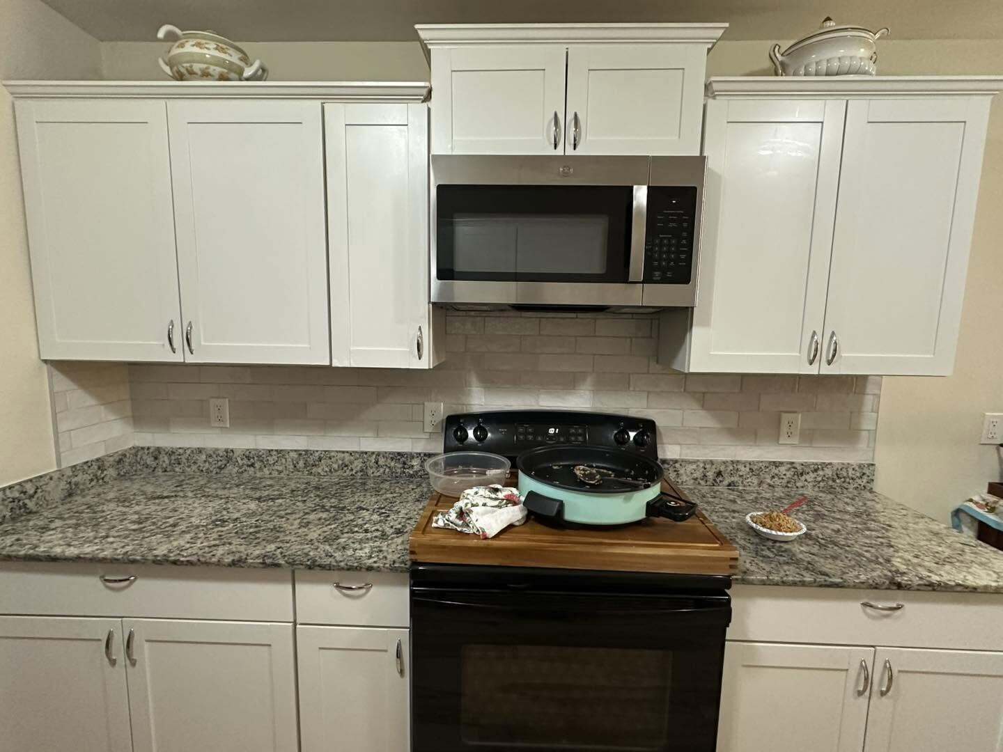 Kitchen with white cabinets, speckled granite counters, tile backsplash, black range and stainless microwave