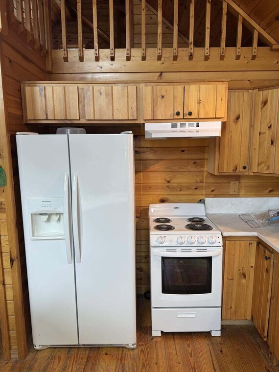 Cabin kitchen with knotty pine cabinets, white side by side fridge and white electric range under loft