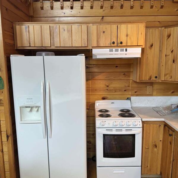 Cabin kitchen with knotty pine cabinets, white side by side fridge and white electric range under loft