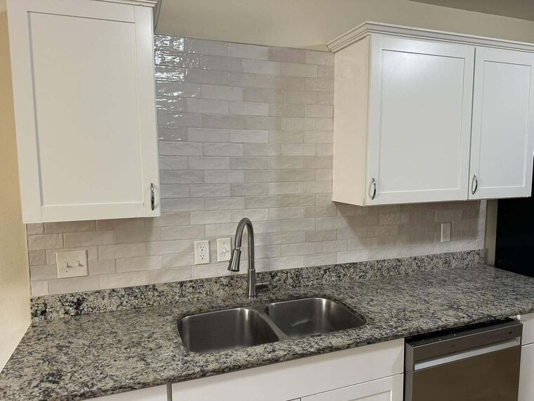 Kitchen with white cabinets, light tile backsplash, speckled stone countertop, double stainless sink and dishwasher