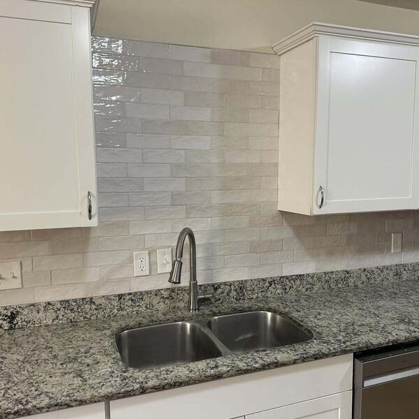 Kitchen with white cabinets, light tile backsplash, speckled stone countertop, double stainless sink and dishwasher