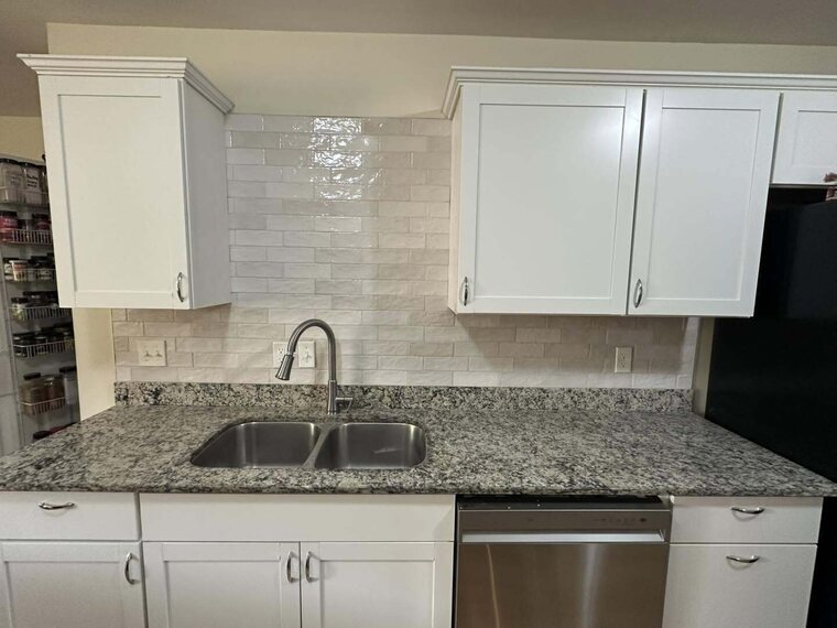 Kitchen with white cabinets, light tile backsplash, speckled stone countertop, double sink and stainless dishwasher