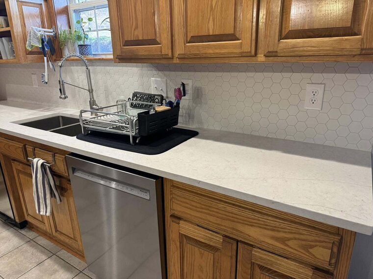 Kitchen with wood cabinets, light countertops, white hexagon tile backsplash, sink, and stainless dishwasher
