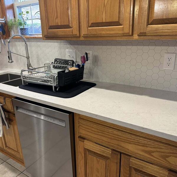 Kitchen with wood cabinets, light countertops, white hexagon tile backsplash, sink, and stainless dishwasher