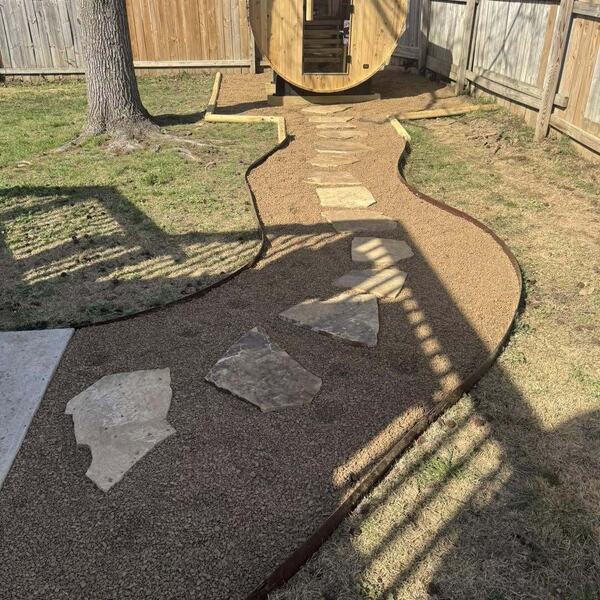 Backyard barrel sauna with curving gravel path and flagstone steppers along wood fence
