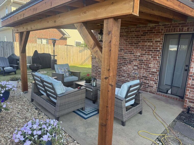 Covered wood patio cover attached to a brick home with wicker patio furniture and potted flowers