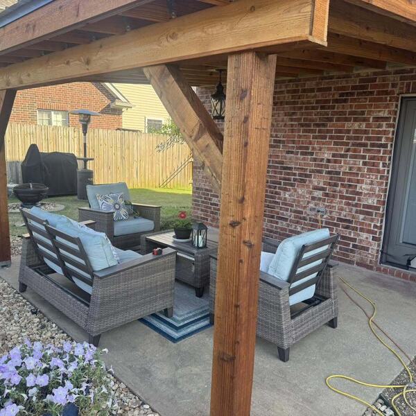 Covered wood patio cover attached to a brick home with wicker patio furniture and potted flowers