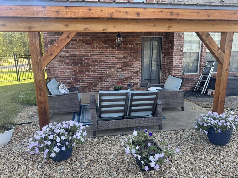 Covered wood patio over a concrete slab with wicker furniture against a brick home
