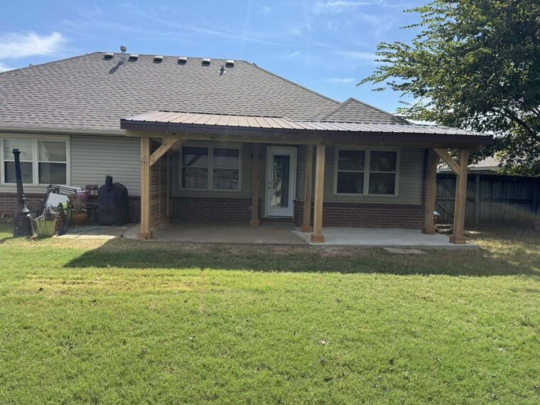 Covered back patio with wood posts and a brown metal roof attached to a brick home