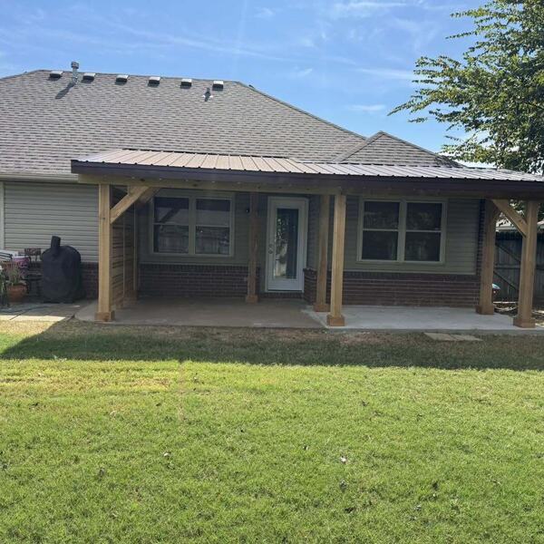 Covered back patio with wood posts and a brown metal roof attached to a brick home