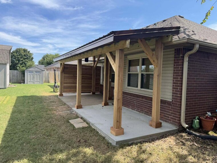 Covered patio with wood post and beam roof attached to a brick home over a concrete slab