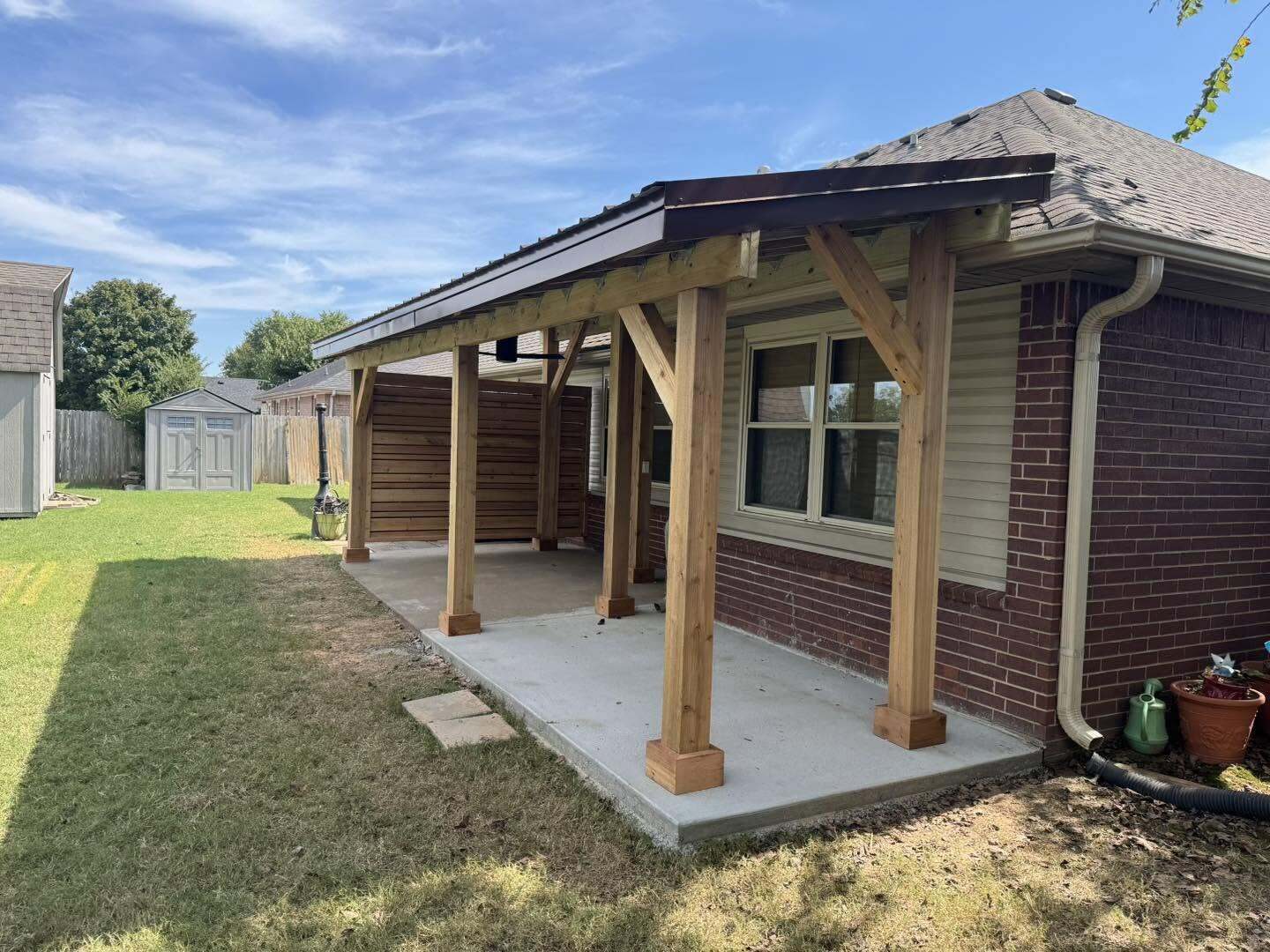Covered patio with wood post and beam roof attached to a brick home over a concrete slab