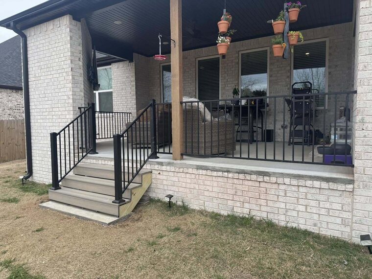 Covered brick porch with black metal railing, steps, hanging flower baskets and patio furniture