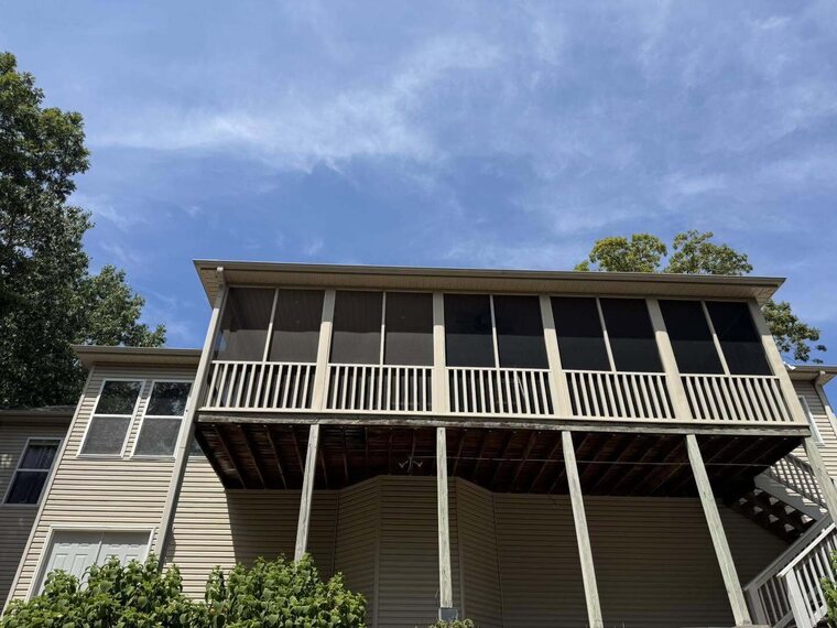 Two story home with an upper level screened porch and railing under a partly cloudy sky