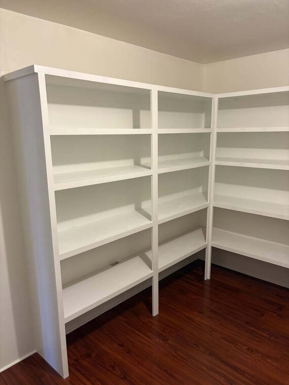 White built in shelving wrapping a corner over dark wood look floor