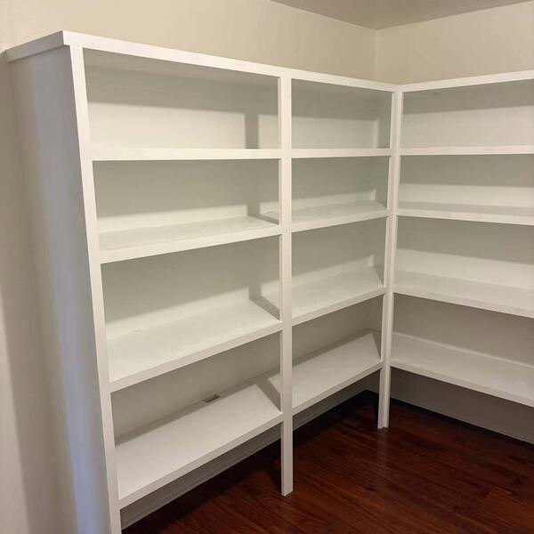 White built in shelving wrapping a corner over dark wood look floor