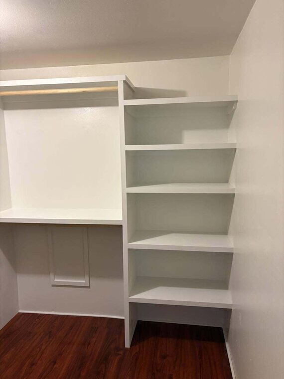 White closet shelving with hanging rod and corner shelves over dark wood look floor