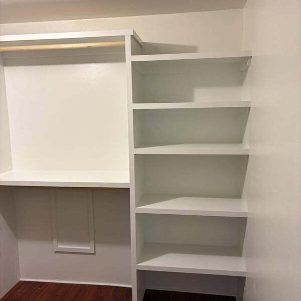White closet shelving with hanging rod and corner shelves over dark wood look floor