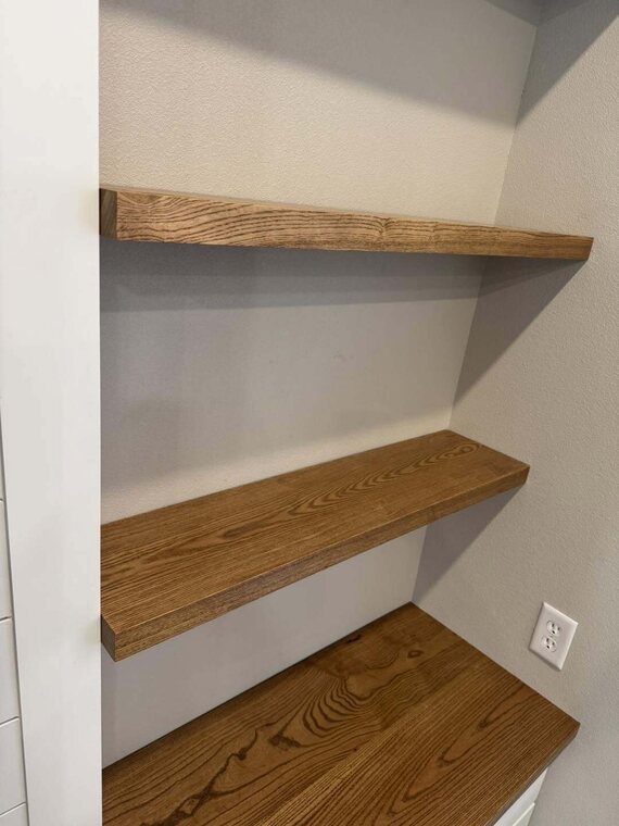 Two stained wood floating shelves and a wood counter installed in a white walled nook
