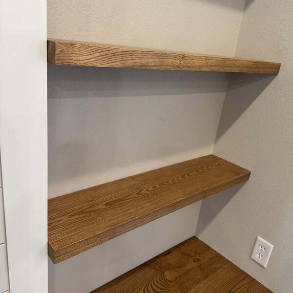 Two stained wood floating shelves and a wood counter installed in a white walled nook
