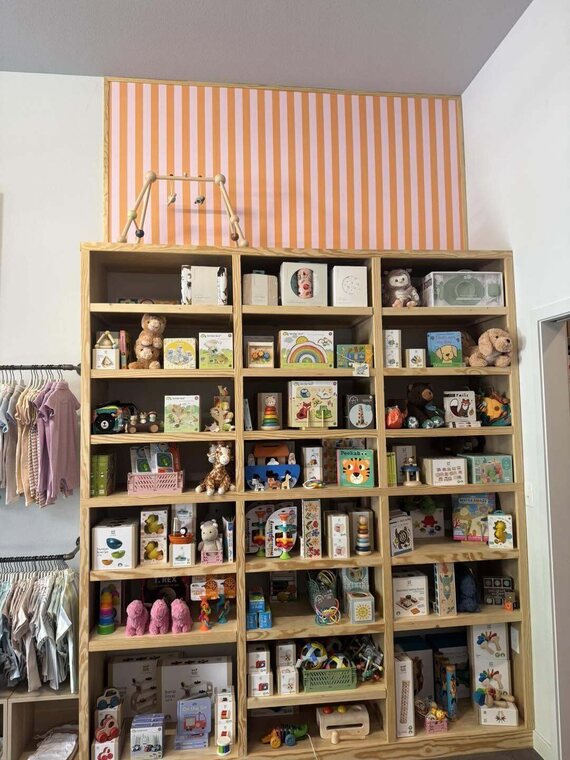 Wood cubby shelving wall filled with toys next to hanging clothing in a shop