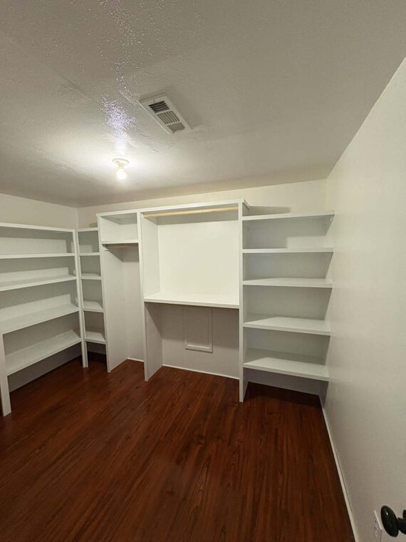 Walk in closet with white built in shelves and hanging rods over dark wood look flooring