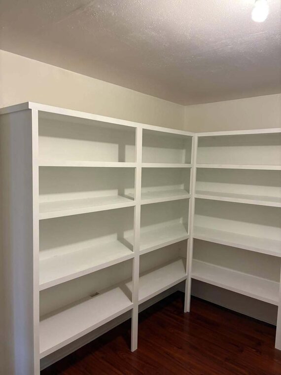Empty white built in shelving wrapping a corner above dark wood floor