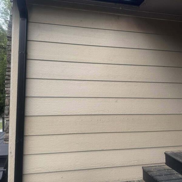Tan lap siding on an exterior wall beside a stone column and dark trim with a wall light