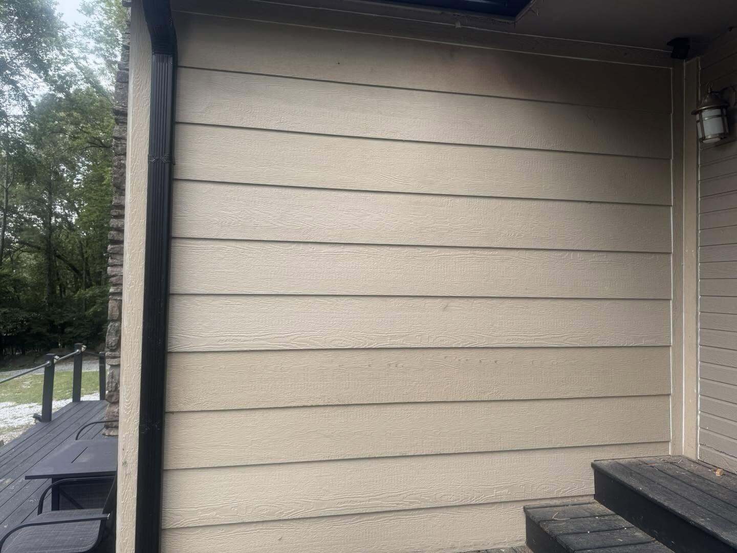 Tan lap siding on an exterior wall beside a stone column and dark trim with a wall light