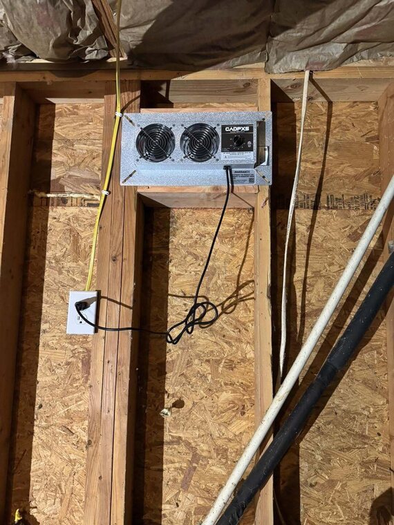 Crawl space ventilation fan mounted to the subfloor among floor joists with wiring and an electrical outlet