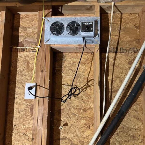 Crawl space ventilation fan mounted to the subfloor among floor joists with wiring and an electrical outlet