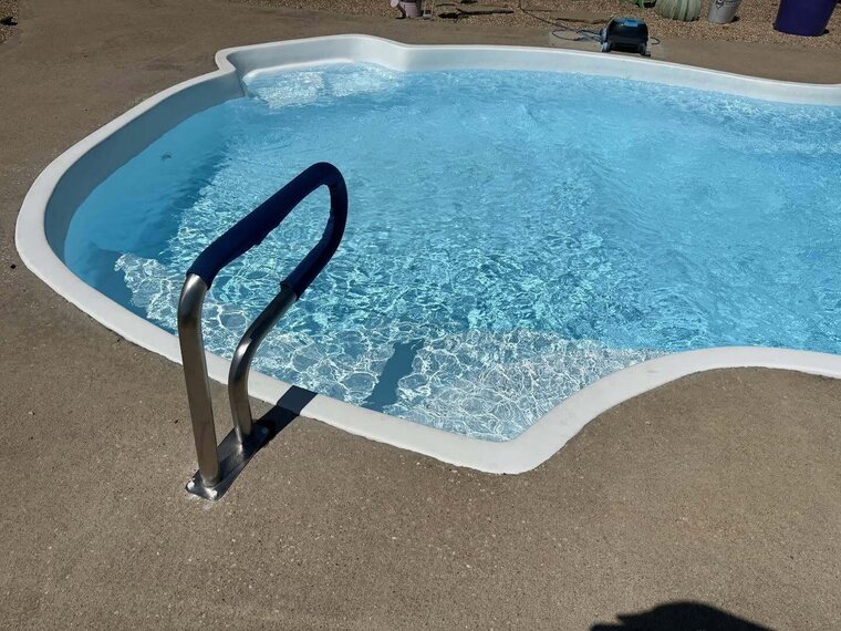 Fiberglass in ground swimming pool filled with clear blue water and a metal entry handrail