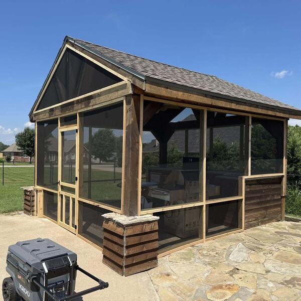 Wood framed screened structure with shingled gable roof on a flagstone patio with a lawn behind